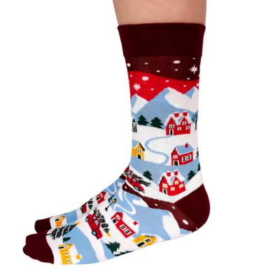 Pair of women's crew socks with a winter village design, featuring colorful red, yellow, and blue houses, snow-covered mountains, and pine trees against a maroon background.
